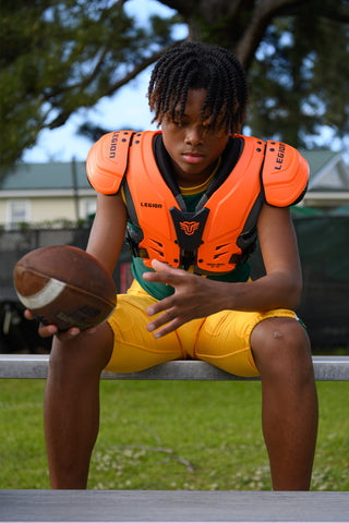 Youth football player wearing LEGION M-80 Highlight Shoulder Pads and holding a football