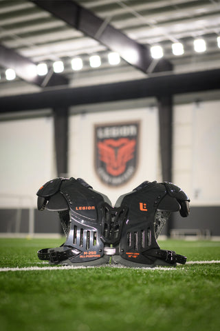 LEGION M-250 Varsity Football Shoulder Pads on a green turf field with a LEGION logo in the background