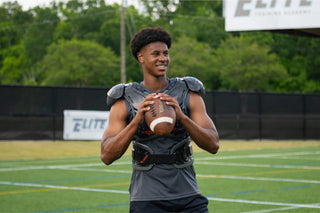 Young man in football pads holding a Wilson football on a green field