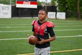 Young boy in black shirt and grey shorts wearing red LEGION M-80 Youth University Football Shoulder Pads