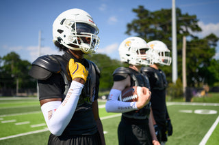 Three football players in helmets and shoulder pads on a field, the first wearing a white LEGION Arm Sleeve