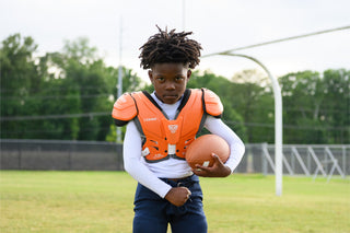 Young boy wearing orange LEGION M-80 Youth University Football Shoulder Pads and holding a football