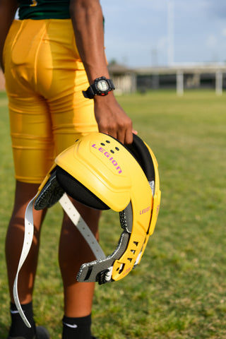 Youth football player in yellow shorts holding a LEGION M-80 Youth University Football Shoulder Pad