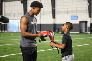 Man handing LEGION M-250 Varsity Football Shoulder Pads to a boy