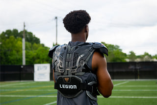 Rear view of a football player wearing black Legion shoulder pads on a green field