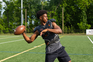 Football player in gray Legion shoulder pads holding a football on a green field