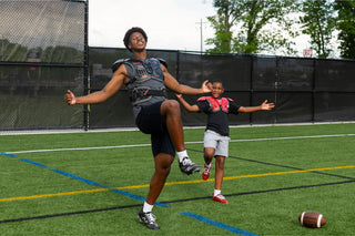 Two football players on a field, one adult and one child, both wearing shoulder pads