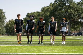 Five football players wearing LEGION M-150 Football Shoulder Pads walk across a green field