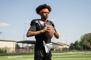 Young male football player wearing a LEGION Headband and shoulder pads, holding a football