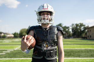 Football player wearing a white Riddell helmet and black Legion shoulder pads, holding a football