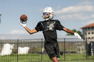 Football player wearing LEGION M-150 Football Shoulder Pads and white helmet catching a football