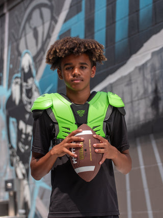 Young boy holding a football in front of a graffiti-covered wall