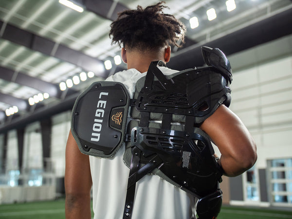 Rear view of a person wearing black Legion football shoulder pads over a white shirt
