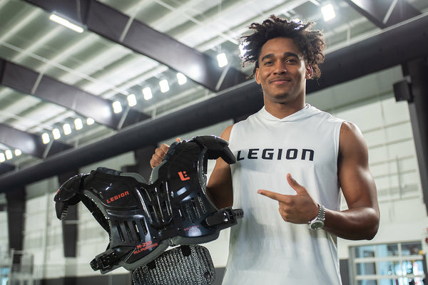 Man in white Legion shirt holding black M-250 All-Purpose shoulder pads