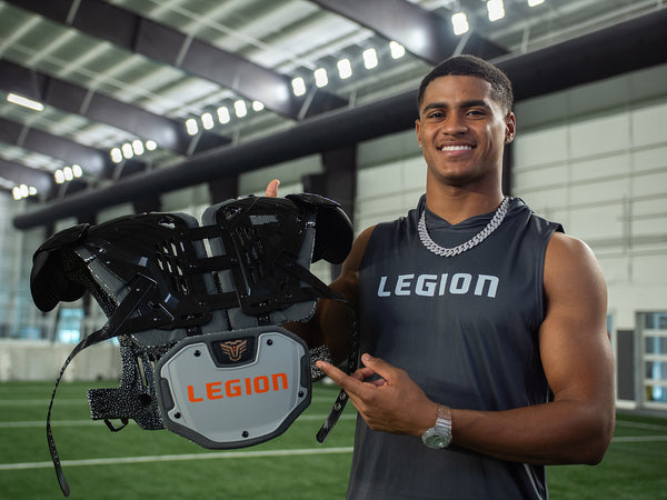 Football player wearing a grey Legion shirt, holding up a Legion shoulder pad