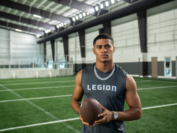 Man in a gray Legion sleeveless shirt holding a football on an indoor turf field