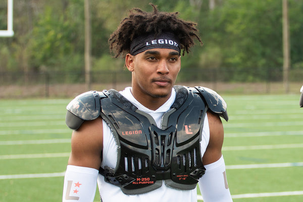 Football player wearing black Legion shoulder pads and headband on a green field